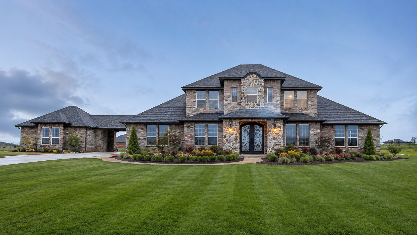 A grand two-story brick and stone custom estate at dusk with an arched iron-door entry